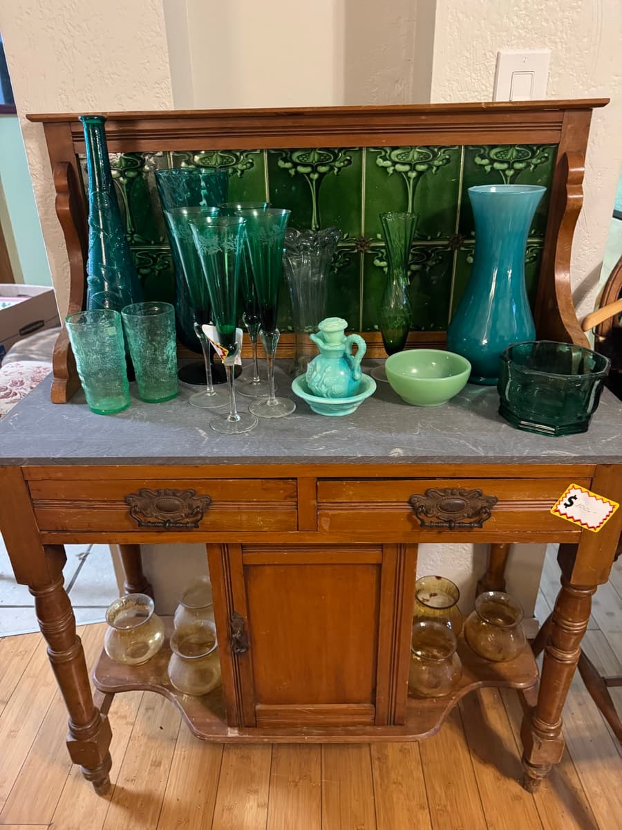 Green glassware collection displayed on an antique wooden cart at an Oregon estate sale